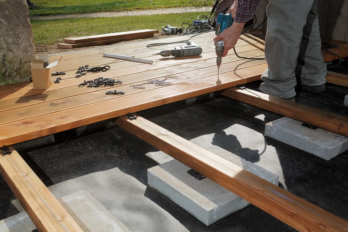 Montage d'une terrasse en bois avec des outils et des fixations visibles, illustration de la construction étape par étape.