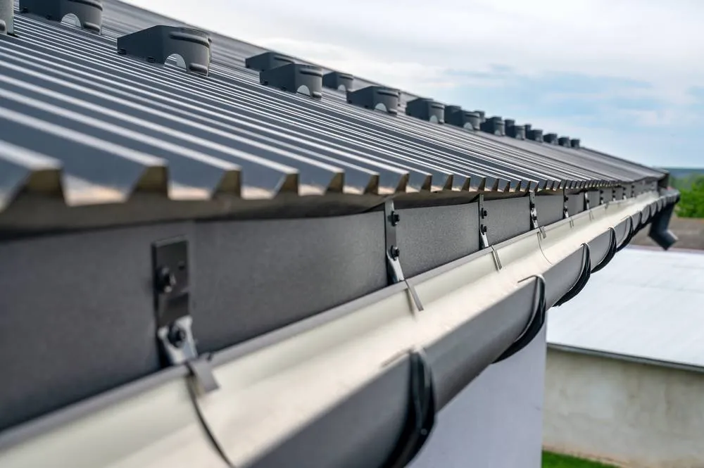 Vue détaillée d'une gouttière en zinc installée sur un toit métallique, illustrant le travail d'un couvreur zingueur.
