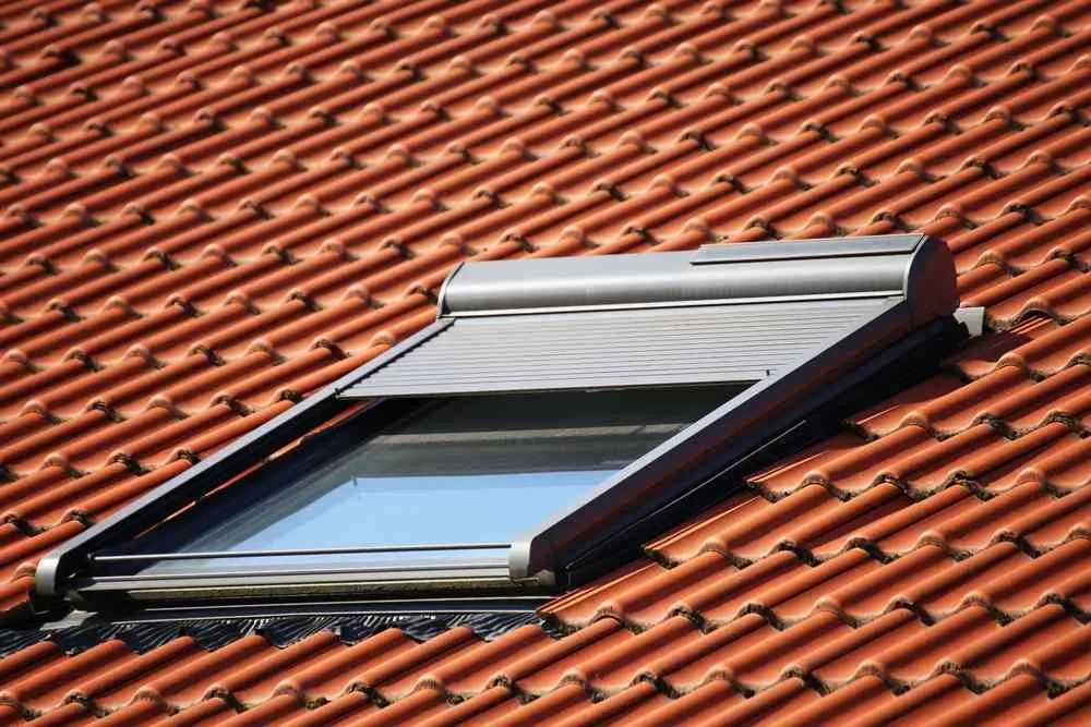 Fenêtre de toit installée avec précision par un couvreur zingueur, intégrée dans une toiture en tuiles rouges. ​​