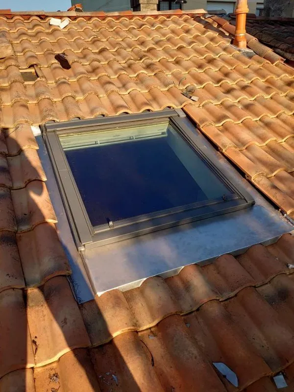 Installation d’une fenêtre Velux carrée sur une toiture en tuiles pour une meilleure isolation et un éclairage naturel.