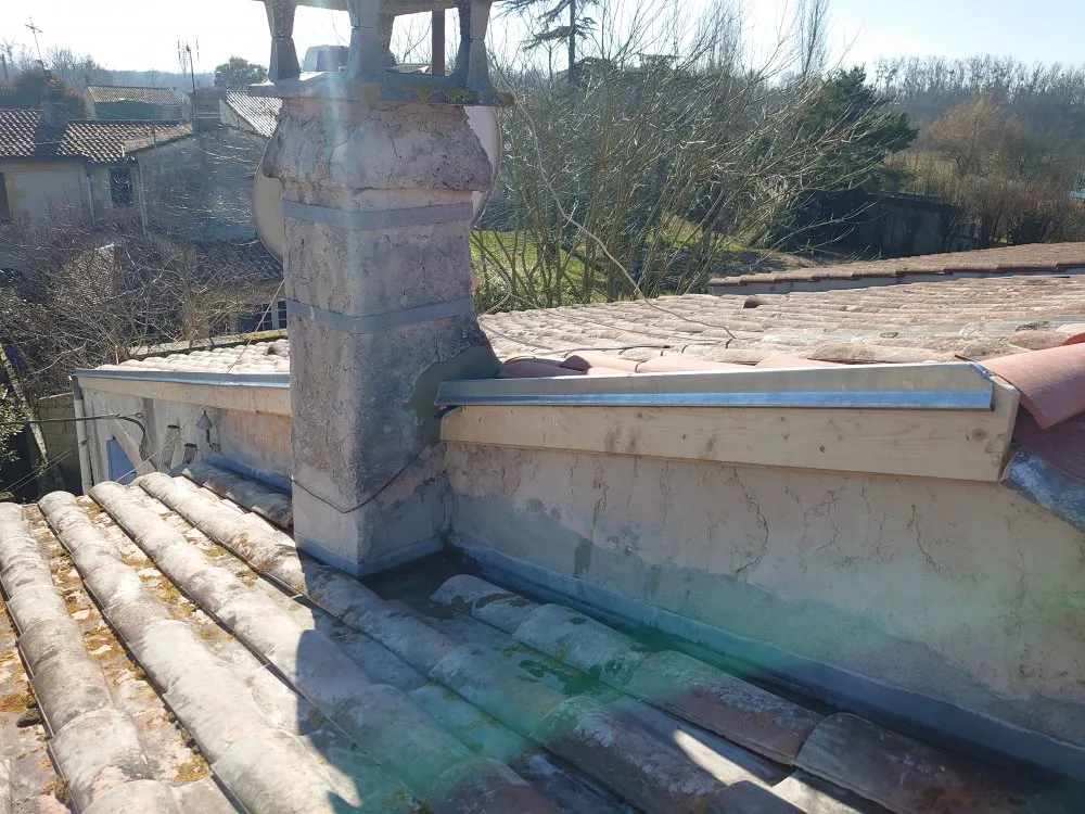 Travail de zinguerie complexe autour d'une cheminée sur un toit en tuiles, dans le cadre de la rénovation d'une toiture.