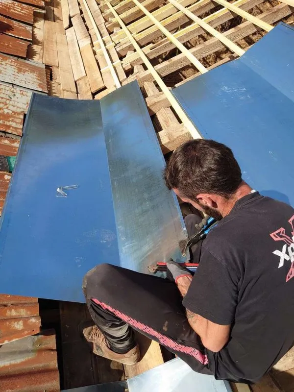 Artisan couvreur travaillant sur la découpe et la pose de plaques de zinc pour la rénovation de toiture.