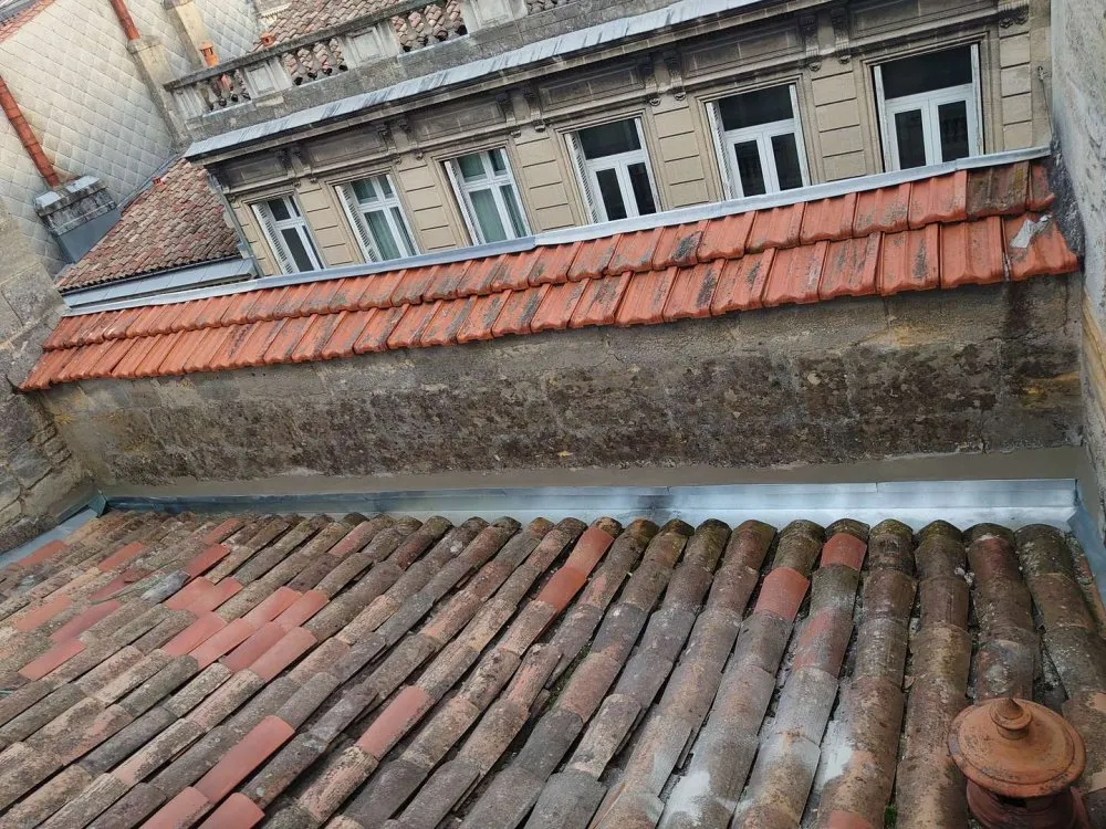 Toiture ancienne en tuiles rénovée avec des éléments de zinguerie pour une meilleure étanchéité.